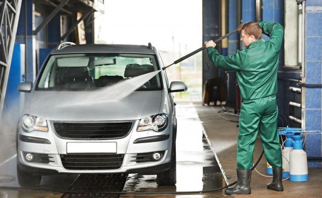 Worker cleaning car with pressured water