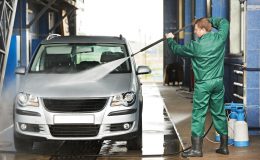 Worker cleaning car with pressured water